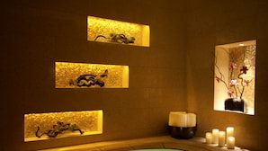 A spa area with a hot tub, wall-mounted decorative panels, candles, and a window with flowers. - The Londoner Hotel (Cotai)