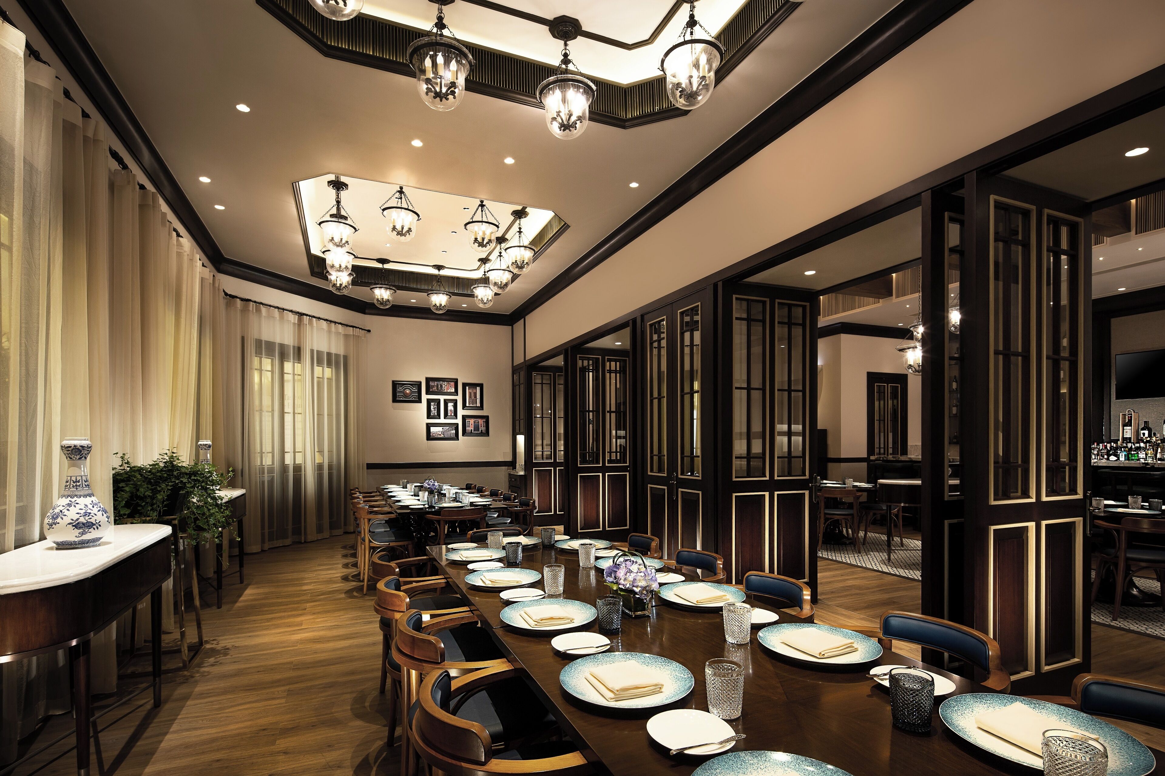 A spacious dining area with a long table set for a meal, elegant chandeliers, and a bar area visible through an open doorway.