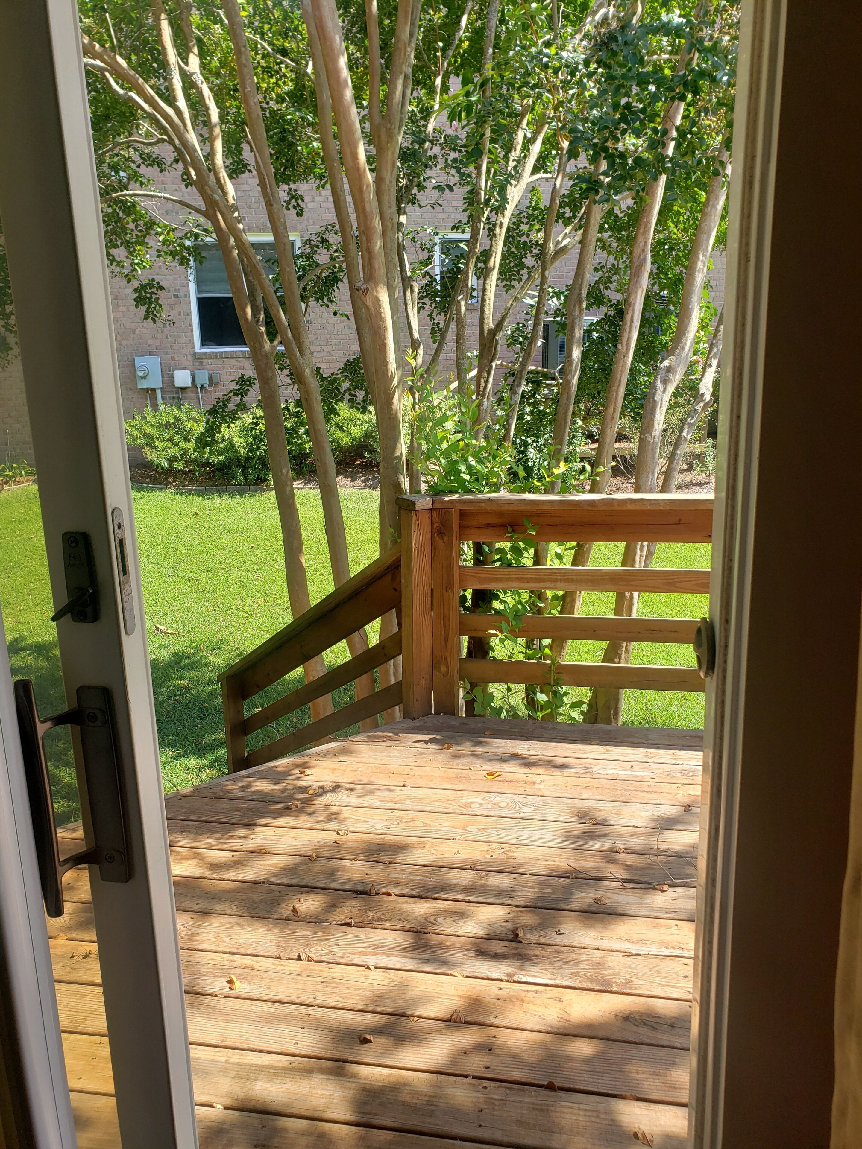 A wooden deck with a railing leading to a grassy area with trees.