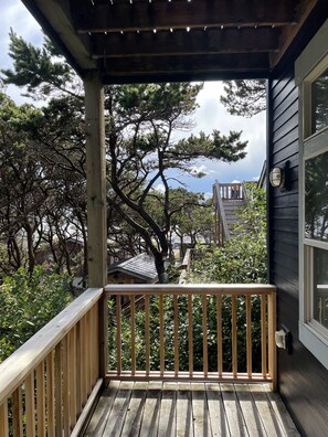 Um deck de madeira com guarda-corpo, com vista para um jardim com árvores e um prédio ao fundo.