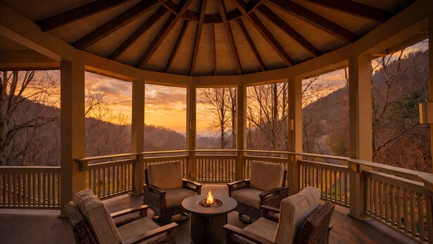 Un espace extérieur aménagé, abrité et doté de chaises en osier et d’un foyer central, offrant une vue sur un paysage montagneux.