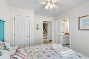 Une chambre à coucher comprenant un lit, un ventilateur de plafond, une porte et un escalier menant à une salle de bain.