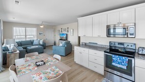 Una cocina moderna con armarios blancos, electrodomésticos de acero inoxidable y un comedor con mesa y sillas.