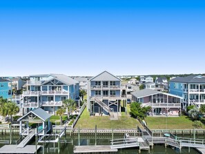 A waterfront residential area with multi-story houses, docks, and a clear blue sky. - NEW to PROACTIVE Vacations! "Tri-D's" is a stunning 6 bedroom, 4 bathroom home WITH elevator! (Holden Beach)