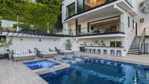 Ett modernt hus i två våningar med en swimmingpool, en uteplats och en bar.