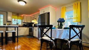 A kitchen with wooden flooring, white cabinets, a refrigerator, and a dining table with chairs.