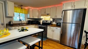 A modern kitchen with white cabinets, a stainless steel refrigerator, a built-in oven, and a wooden floor.