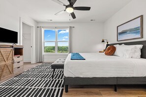 A bedroom with a bed, a ceiling fan, a TV, a window with a view, and a desk with drawers.