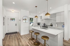 A modern kitchen with white cabinetry, a central island with stools, pendant lighting, and a view into the adjacent living area.