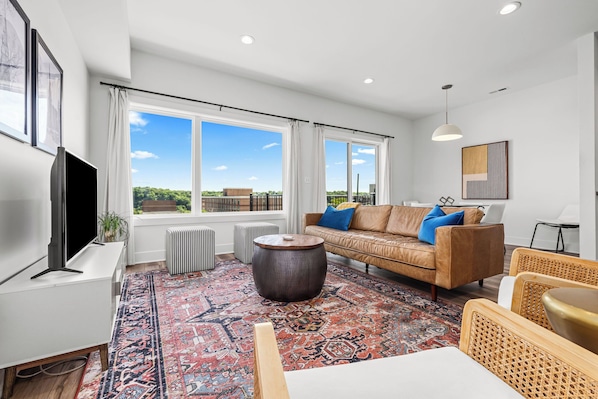 A modern living room with a large window, a sofa, a coffee table, and a television.