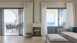 A modern living room with a sofa, a small table, and a fireplace. There is a balcony with a view of the sea. - Brand new house on the beach with panoramic views and a pool (Son Serra de Marina)