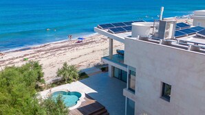 A modern building with a rooftop pool and solar panels, overlooking a beach with clear blue waters and distant mountains. - Brand new house on the beach with panoramic views and a pool (Son Serra de Marina)