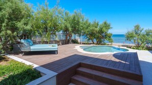 A wooden deck with a hot tub, a blue sofa, and a view of the sea. - Brand new house on the beach with panoramic views and a pool (Son Serra de Marina)