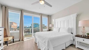 Una camera da letto con un letto grande, un ventilatore a soffitto, un comodino con lampada, una cassettiera e vista sulla città.