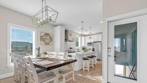 Una cucina moderna con mobili bianchi, un'isola centrale, luci a sospensione e una zona pranzo con sedie bianche.