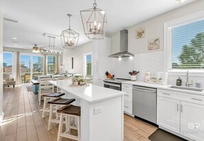 Une cuisine moderne avec des meubles blancs, un îlot central, des luminaires suspendus et une vue sur l’extérieur.