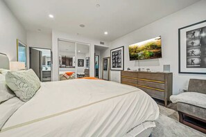 Un dormitorio moderno con una cama grande, un aparador, un espejo y un televisor.