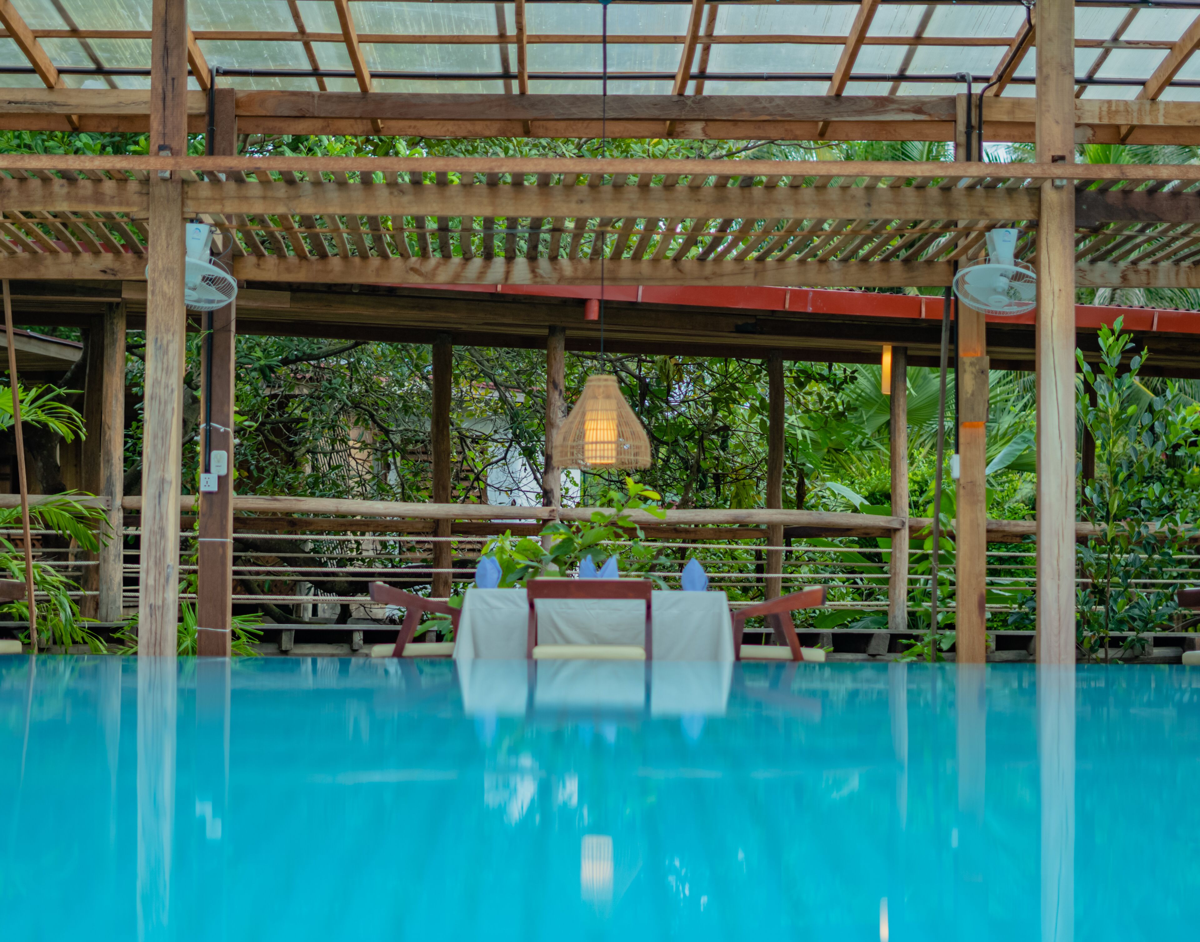 Un área de piscina con una pérgola de madera, sillas de descanso y una lámpara colgante.