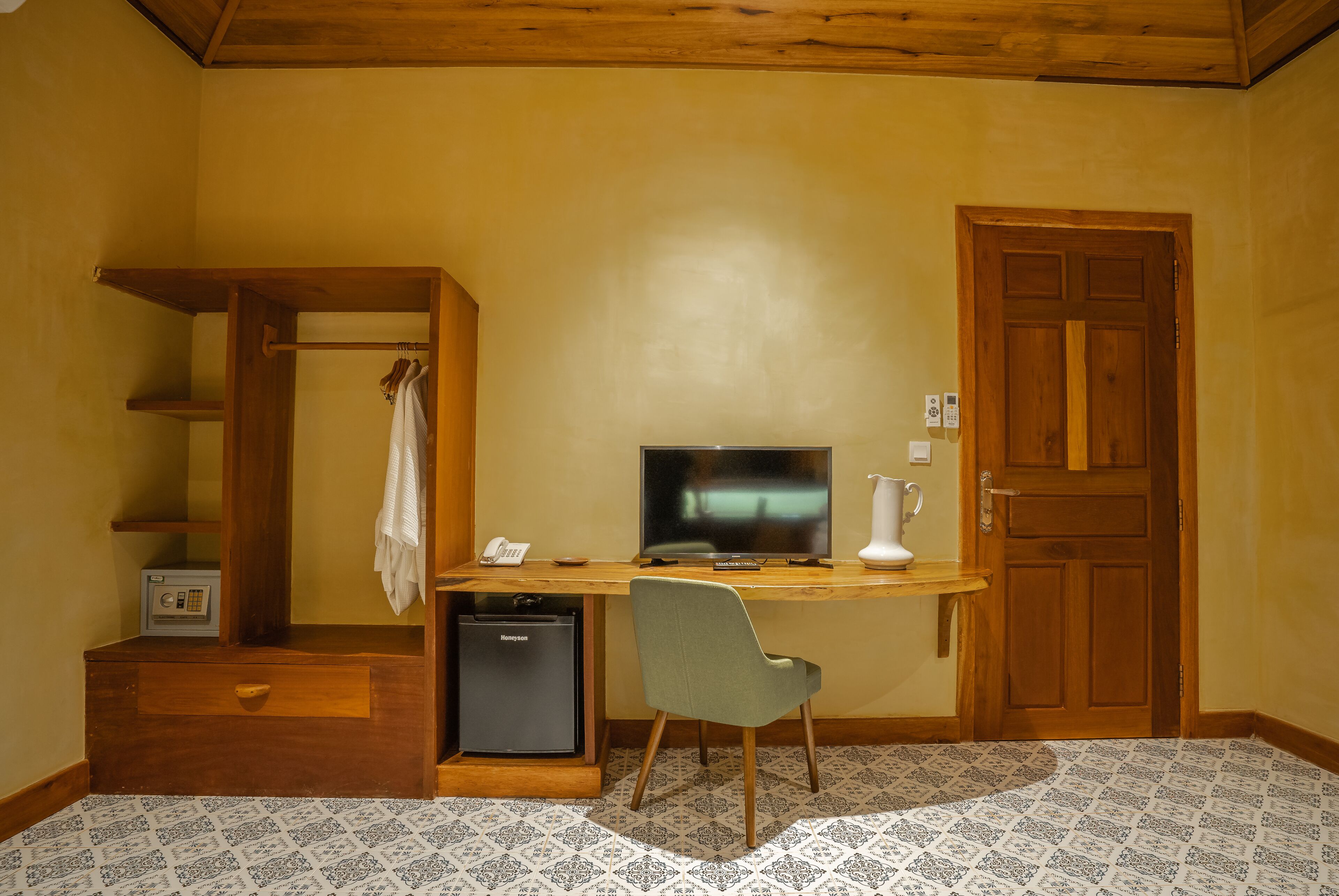 A compact room with a wooden desk, a television, a small refrigerator, a chair, and a door.