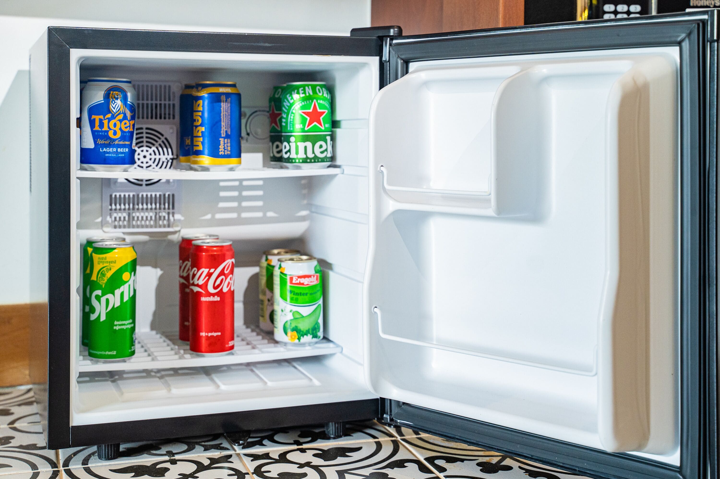 Een open koelkast met diverse dranken, waaronder Tiger Lager Bier, Heineken, Sprite, Coca-Cola en Ergotell.