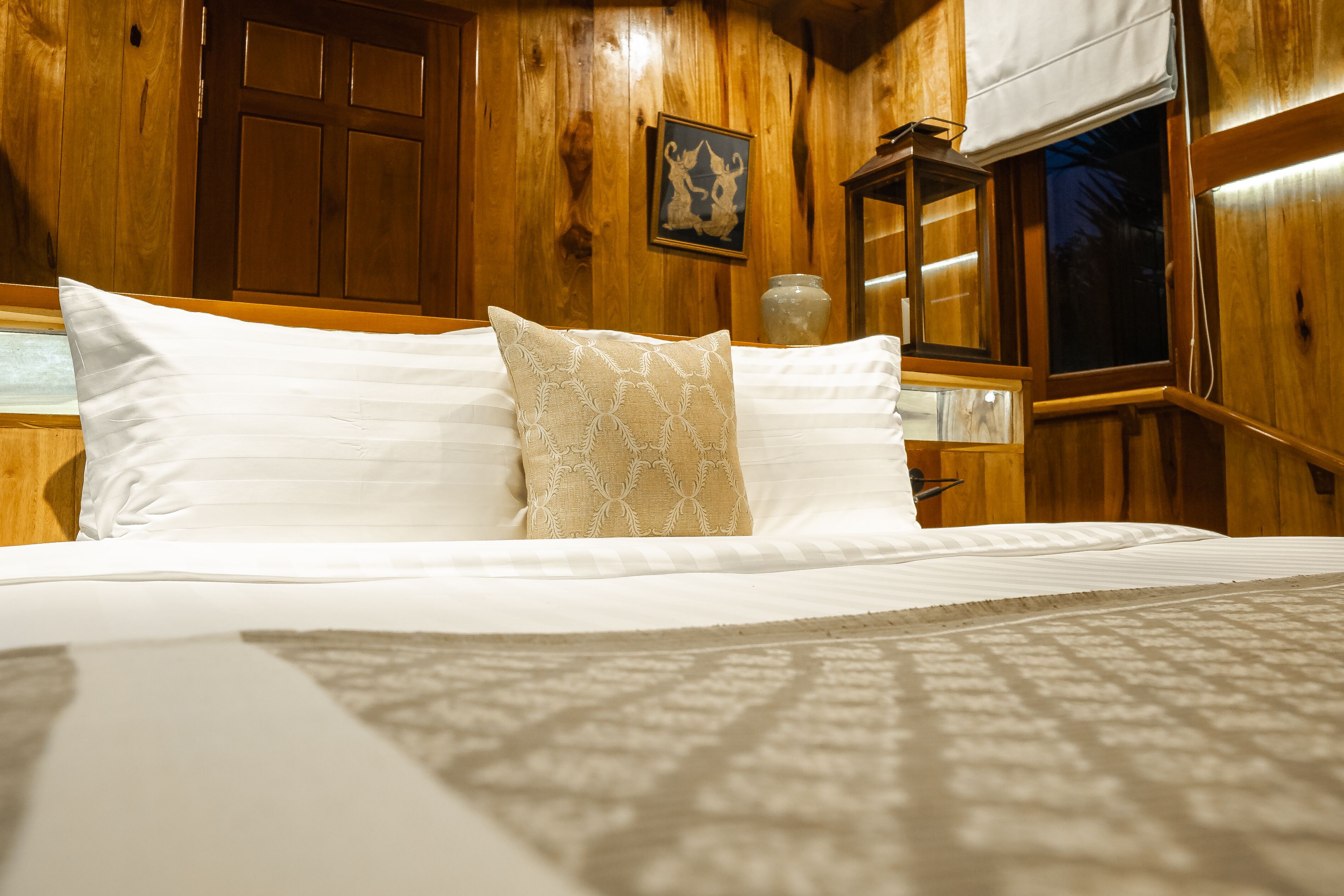 A wooden-paneled room with a bed, a framed picture on the wall, and a window with a view.