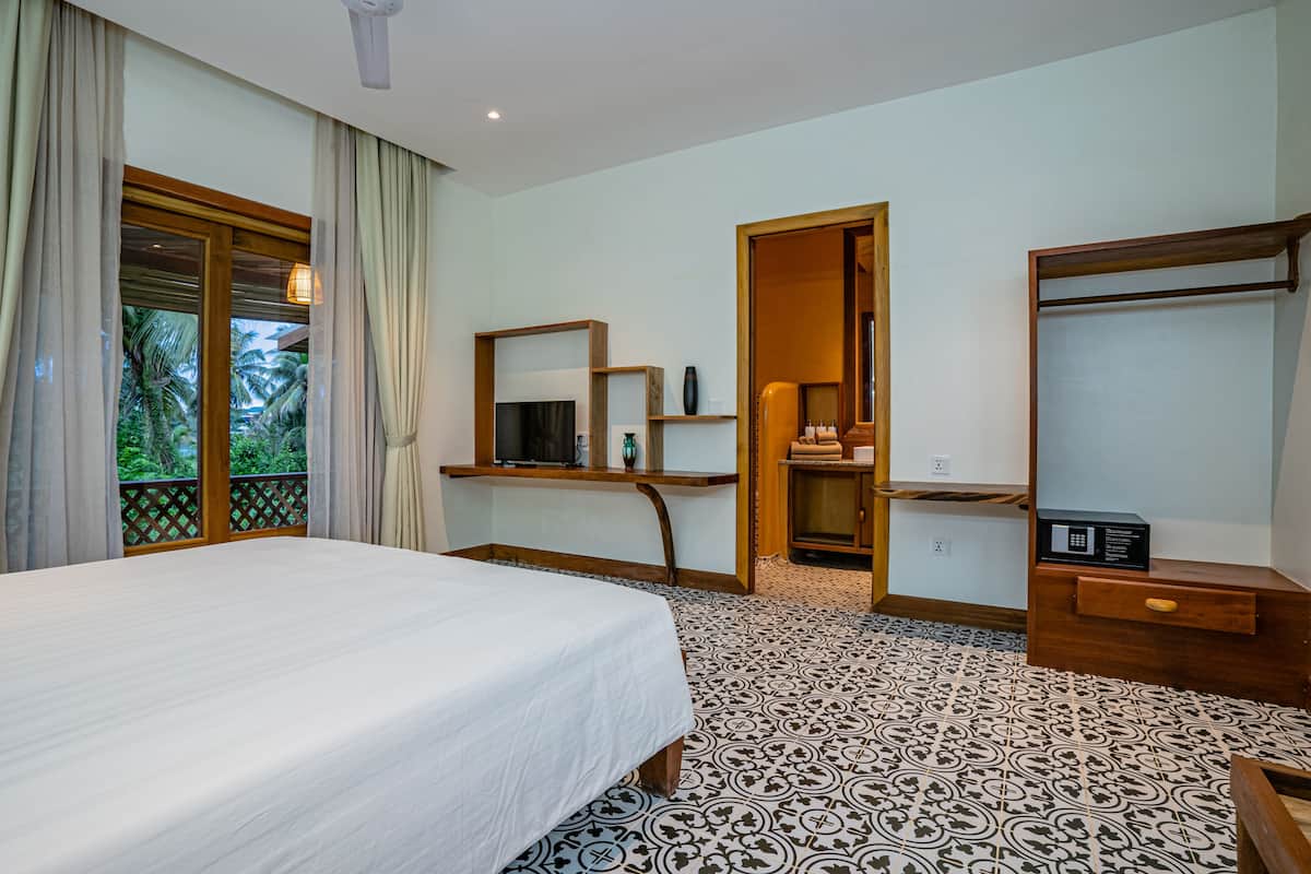 A bedroom with a large bed, a wooden desk, a mirror, and a wardrobe.