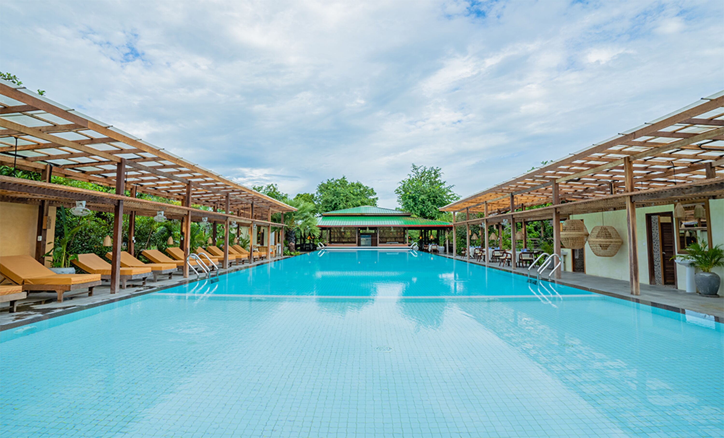 A large indoor swimming pool with wooden pergolas and lounge chairs on either side.