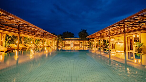 A pool area with tiled flooring, lounge chairs, and wooden pergolas. - Peam Snea Resort (Kampot)