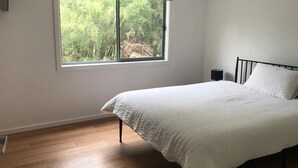 A bedroom with a bed, a window with a view of trees, and a bedside table with a lamp. - Tenscott in Halls Gap (Halls Gap)