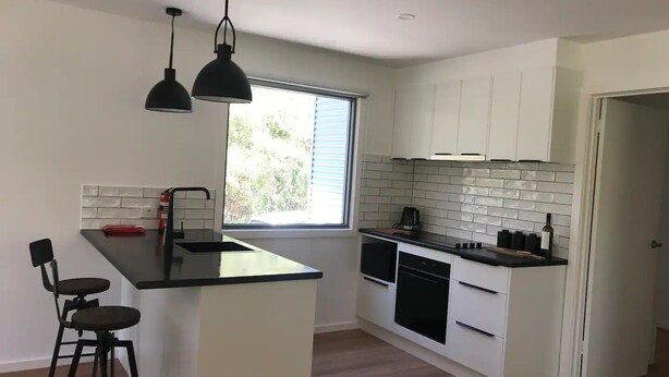 A modern kitchen with white cabinets, a black countertop, and a window providing natural light. - Tenscott in Halls Gap (Halls Gap)