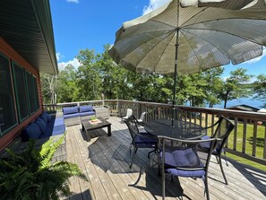 Relax on the deck with a sofa, table, and chairs, surrounded by trees and a serene water view.