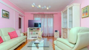 A living room with a sofa, armchair, glass coffee table, television, and a cabinet.