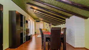 A dining area with a wooden table and chairs, a brick wall, and a ceiling with exposed beams.