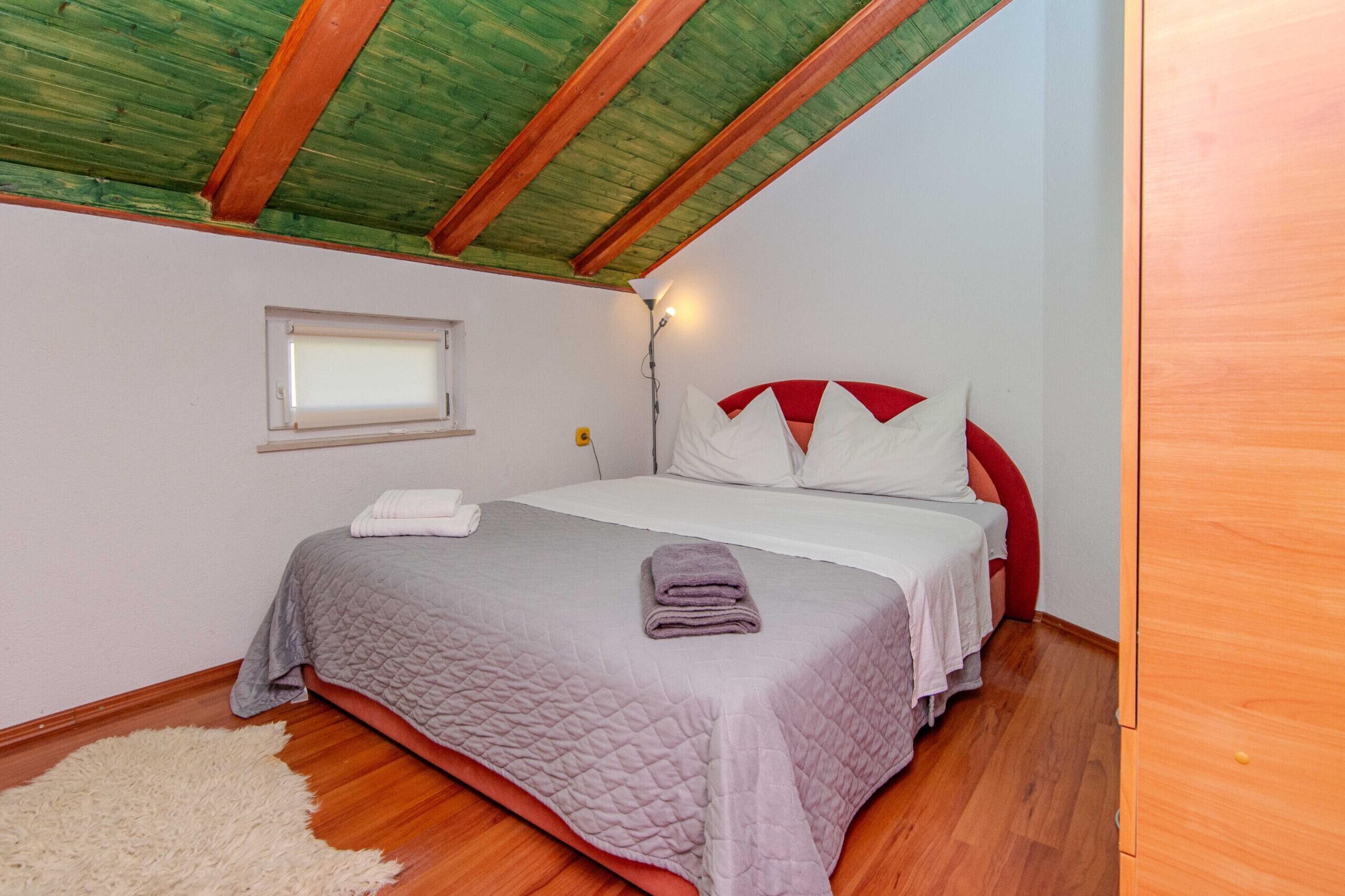 Ein Schlafzimmer mit einem Bett, einem Fenster, einem Nachttisch und einer Holzbalkendecke.
