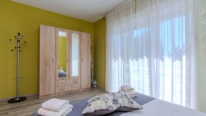 A bedroom with a bed, a wardrobe, a coat rack, and a window with sheer curtains.