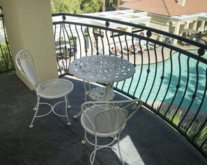En balkon med et bord og to stole, med udsigt over en swimmingpool.