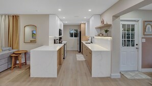 Eine moderne Küche mit weißen Schränken, einer zentralen Kochinsel und einem Essbereich mit grauem Sofa und Holztisch.