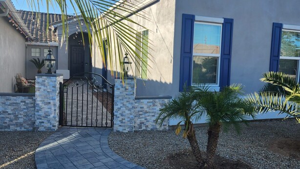 A modern house with a stone and stucco exterior, a curved driveway, and a palm tree in the yard.