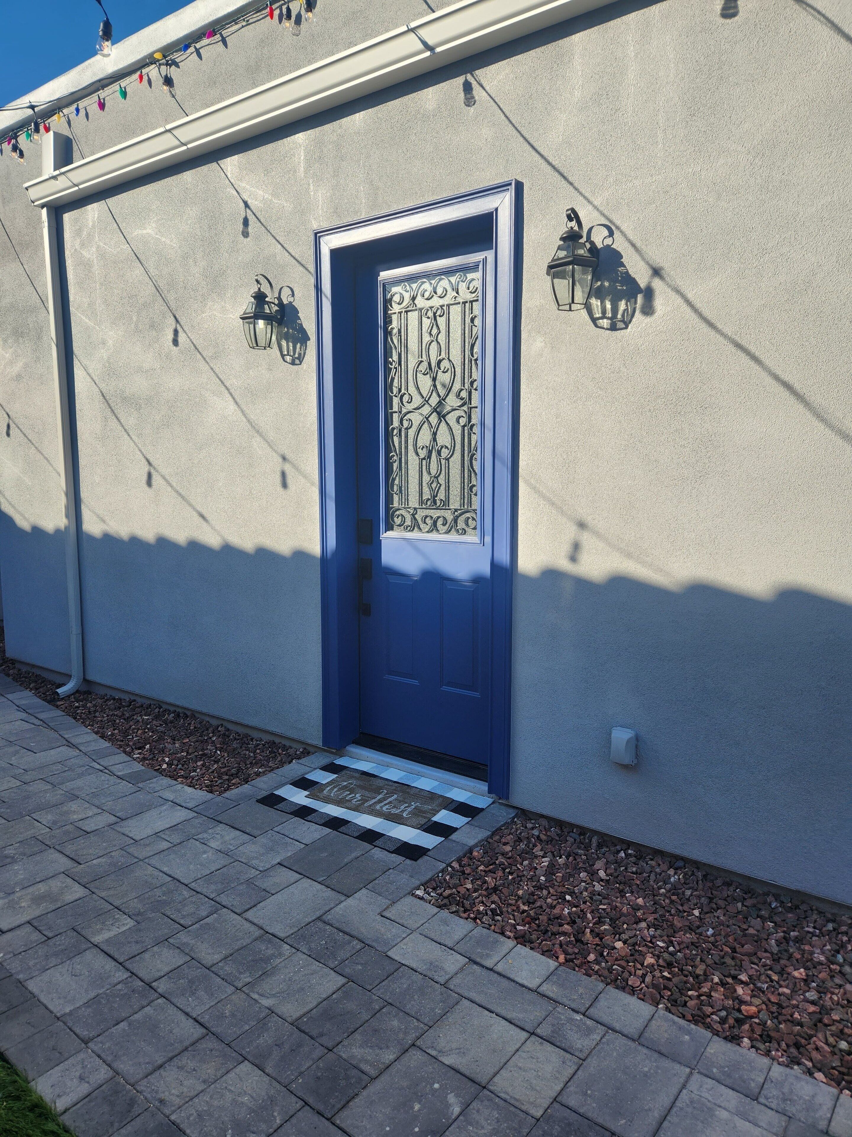 Una puerta azul con detalles de metal decorativo, un escalón pequeño que lleva a ella y un felpudo con el texto 'Car Nest'.