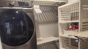 A laundry area with a front-loading washing machine and dryer, a drying rack, and shelves with laundry supplies.