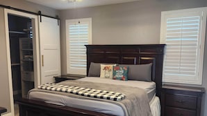 A bedroom with a large bed, a ceiling fan, a nightstand, a dresser, and a closet with sliding doors.