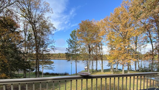 A lakeside view from a deck with a railing, trees with autumn foliage, and a clear sky. - Stunning views on tranquil lake. (Crosslake)