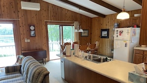 A cozy cabin-style kitchen with a central island, wooden walls, and a dining area with plaid-patterned furniture. - Stunning views on tranquil lake. (Crosslake)