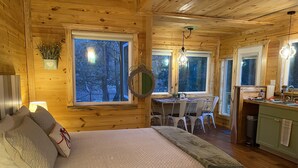 Interior acogedor de una cabaña con cama, mesa de comedor, sillas y zona de cocina.
