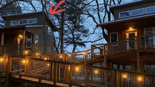 Una cabaña de madera con terraza y varias ventanas, rodeada de árboles.