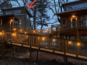 Une cabane en bois dotée d’une terrasse et de nombreuses fenêtres, entourée d’arbres.
