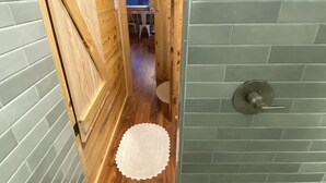 Un pasillo estrecho con paredes de madera y suelo de baldosas, que conduce a una habitación con una puerta y un pequeño tapete redondo.