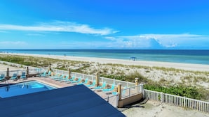 Une vue sur la plage avec un espace piscine, des chaises longues et une plage de sable.