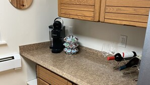 Una cocina con armarios de madera, una cafetera Keurig, un portalápices para café, botellas de vino y vasos.
