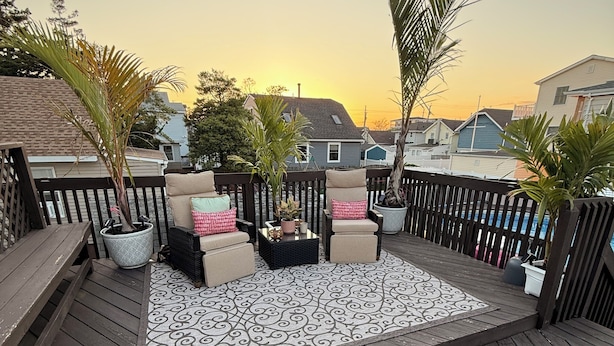 Una terraza de madera con mobiliario exterior, plantas en macetas y un tapete estampado.